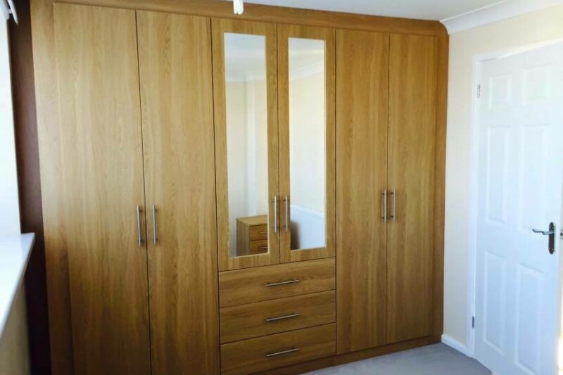 Wood finish fitted wardrobe in Bournemouth with three drawers and mirrored doors
