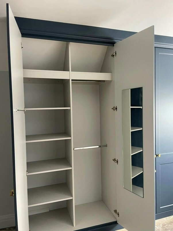 Bespoke fitted wardrobes with hinged doors open to reveal custom internals with shelves, mirror, and hanging rail