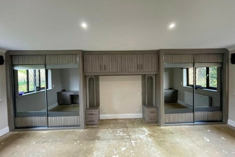 Large fitted bedroom furniture including two sliding door fitted wardrobes and over-bed storage in dark wood and glass